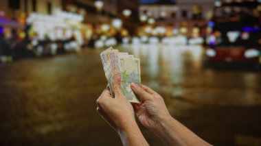 Bir adamın elleri Romen leu banknotlarını bir şehir sokağında tutuyor, canlı bir şehirde para birimini gösteriyor..