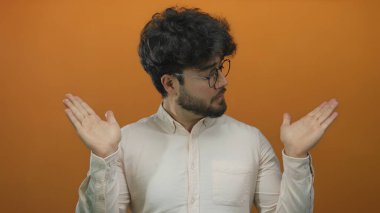 Genç İspanyol sakallı, elleri dışa doğru uzanan canlı turuncu arka plan gözlüklü ve beyaz gömlekli üç karede kafa karışıklığı ya da belirsizlik gösteren genç bir adam..