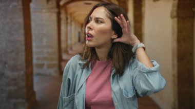 Üniversite koridorundaki kadın dikkatle dinliyor, merak ve mimari ortama olan ilgisini çekiyor..