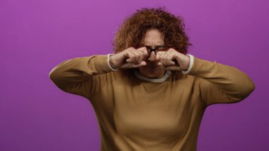 Gözleri ovalayan bir kadın, parlak pembe duvarın üzerinde şüpheli görünüyor. Gözlüklü, kahverengi süveter giyiyor. Orta yaşlı, esmer, ispanyol izole edilmiş, inançsızlık ifadesi sergiliyor..