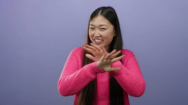 Mor arka planda pembe süveter giyen, el hareketleriyle gülümseyen, neşe ve ifadeyi somutlaştıran bir kadın..