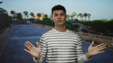 Bir şehir sokağında el kol hareketi yapan genç adam, açık bir şehir ortamında ihtiyatını dile getiriyor..