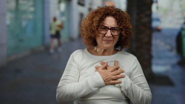 Dışarıda göğsü açık bir kadın, şehir sokaklarında dikiliyor. Bulanık şehir geçmişiyle ilgili endişeleri var. Acil bir durum ya da sorun var gibi görünüyor..