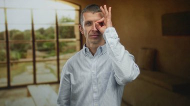 Oteldeki adam göze yakın, kapalı mekanda, tarafsız ifadeli, bulanık arka planda, sıradan bir çevreyi gözler önüne seriyor..