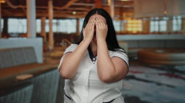 Kapalı alanda gülümseyen kıvrımlı bir kadın, modern bir otel ortamında eğleniyor, neşeli hareketleriyle neşeli duygularını ifade ediyor, sofistike atmosferi aydınlatıyor..