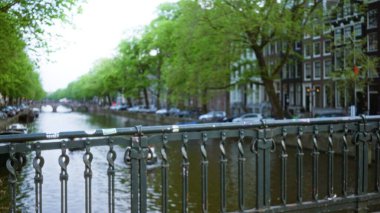 Bulutlu bir gökyüzü altında çözünmüş ağaçları ve tarihi binaları olan bulanık kanallar, ikonik Hollanda mimarisi ve şehir manzarası sergiliyor..