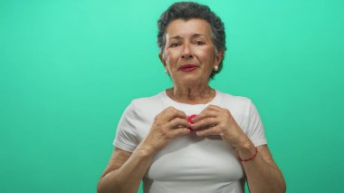 Gri saçlı yaşlı kadın yeşil arka planda kırmızı kalbi tutuyor, özen ve samimiyetini ifade ediyor..