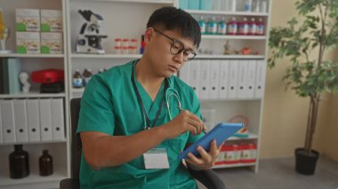 Bir klinikte genç bir doktor, modern bir tıbbi iş yerinde konsantrasyon ve teknolojiye odaklanmış bir tablet kullanıyor.