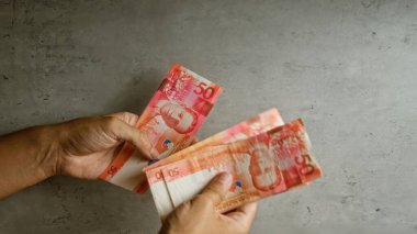 Elinde filipin pesolarını tutan ve sayan bir adam var.