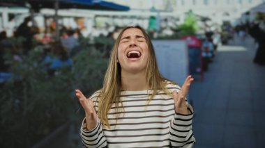 Açık hava restoranının terasında duygularını elleriyle ifade eden, hareketli sokak sahneleriyle çevrili, şehir ortamında samimi anlar yakalayan bir kadın..