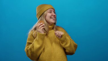 Kurabiyeli, sarı kazaklı, mavi arka planda şapkalı neşeli ve mutlu bir kadın..