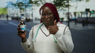 Şehrin sokaklarında bir kadın elinde ilaç şişesi, boynunda steteskopla baş parmak işareti yapıyor ve dışarıda sağlığa teşvik ediyor..
