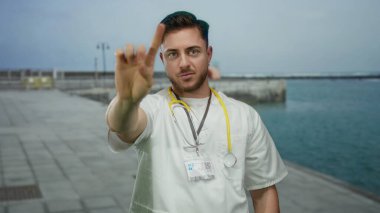 Steteskoplu beyaz önlüklü genç sakallı doktor deniz kenarında okyanus manzaralı gezinti yapmaz.