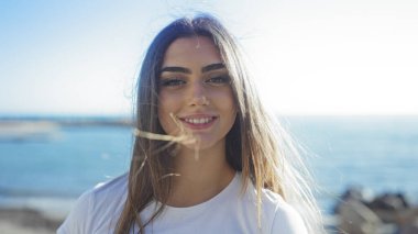 Güneşli deniz kıyısında arka planda suyla gülümseyen bir kadın güzelliği ve kaygısız açık hava yaşam tarzını ön plana çıkarıyor..