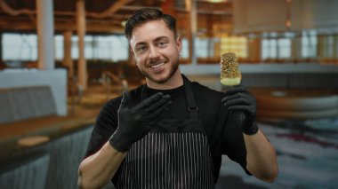 Önlüklü genç adam restoran ortamında dondurma tutuyor. Hoş bir gülümseme sergiliyor..