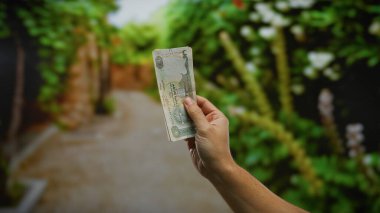 Canlı bir park ortamında el ele tutuşan Dirham banknotu, para ve finans temaları vurgulanıyor..