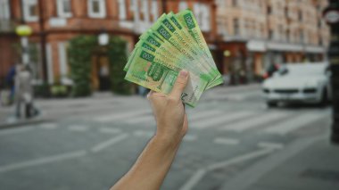 Şehir ortamında elinde Rus rublesi tutan adam, bulanık yayalar ve binalarla şehir geçmişine karşı belirgin bir para birimi sergiliyor..