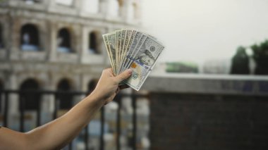 Roma 'daki Roma Kolezyumu' nun önünde para ve ikonik simgeler üzerine kurulu bir seyahat teması sergileyen bir adam bize dolar tutuyor..