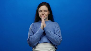 Esmer kadın, mavi arka planda meditasyon yapıyor. Rahat bir ifade, sakin bir atmosfer ve huzurlu bir ortamda gözleri kapalı.