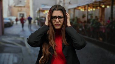 Gözlüklü genç İspanyol kadın açık hava yemekleri ve bulanık yayaları olan canlı bir şehir caddesinde stresli görünüyor..