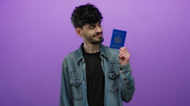 İzole edilmiş mor duvara karşı Küba pasaportu tutan, sıradan kot giyimli, modern keşif ruhunu temsil eden, kimlik ve seyahat temaları sergileyen bir adam..