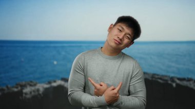 Sahil kenarında sakin bir sahilde, temiz gökyüzünün altında düşünceli bir ifadeyle poz veren genç adam..