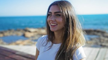 Kadın, güneşli bir günde dalgalı okyanus arkaplanıyla sahil sahnesinin dinginliğini ve güzelliğini artırmak için öylesine gülümsüyor..