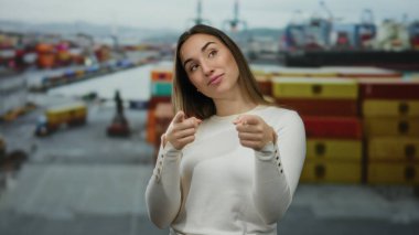Renkli nakliye konteynırları ve deniz manzarası ile çevrili bir liman ortamında neşeli bir gülümsemeyle kameraya bakan kadın, neşe ve deniz macerasının somutlaştırıcısı..