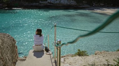 Mallorca 'daki Cala Llombards plajında turkuaz denizde dinlenen, çarpıcı Akdeniz manzarasına bakan, parlak güneş ışığı altında huzurlu tatil anlarının tadını çıkaran bir kadın..