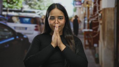 Kalabalık bir sokakta, gözleri kapalı meditasyon yapan bir kadın, sakin bir yüz ifadesi sergiliyor, dinamik bir şehirde dinginliği vurguluyor..