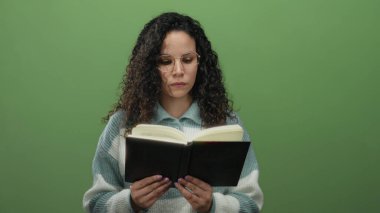 Yeşil duvar arka planında kitap okuyan, gözlüklü, çizgili kazaklı, odaklanmış ve entellektüel ambiyansı olan bir kadın..