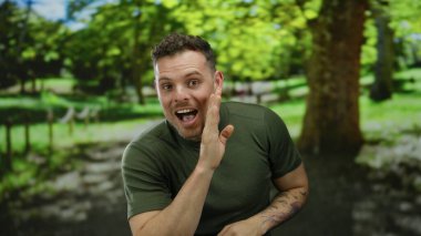 Dövmeli genç adam açık havada, yemyeşil bir parkta neşeli bir fısıltıyla neşeli ve güneşli bir atmosferle çevrili doğal bir ortamda mutluluk ve cazibe yayıyor..