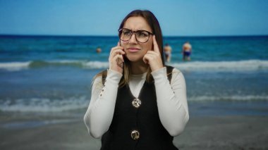 Sahilde duran, stresli, telefonda konuşan, deniz kenarında güneşli bir günü sakin bir ufukla yakalayan, gözlüklü, sıradan görünümlü bir kadın..