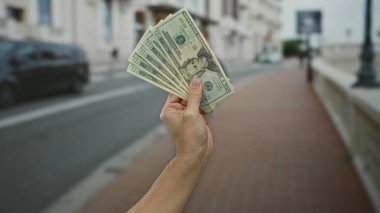 Bir şehir caddesinde Amerikan dolarlarını elinde tutan adam, bulanık bir şehir geçmişiyle açık havada para sergiliyor, açık bir ortamda finans ve zenginliği vurguluyor..