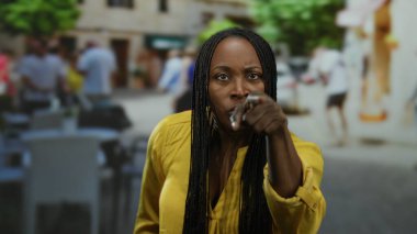 Örgülü bir kadın açık bir terasta, hareketli bir şehir kafesinde, güneşli bir günde şehir hayatının özünü ve hayat dolu sokak enerjisini yakalıyor..