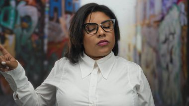 Şehir sokaklarında kendine güveni tam bir kadın, güçlü, iddialı bir tavır sergiliyor, el hareketi, kalın çerçeveli gözlükler ve ciddi bir ifadeyle kendini gösteriyor..