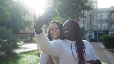 Güneşli bir günde şehir parkında selfie çeken iki kadın arkadaş neşe ve dostluğu yakalıyorlar..