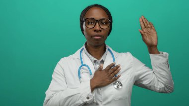 Steteskoplu bir kadın, yemin ya da bağlılık jesti için yeşil arka plana el kaldırıyor..