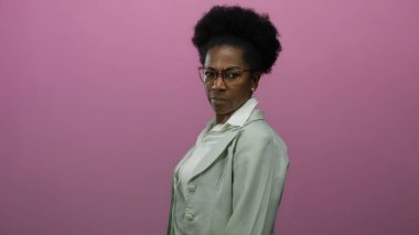 İzole edilmiş pembe arka plana karşı duran, beyaz gömlek üzerine gözlük ve ceket giyen bir kadın.