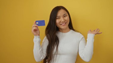 Sarı arka planda elinde kredi kartı olan gülümseyen bir kadın mali bağımsızlığını ve modern bankacılığı gösteriyor..
