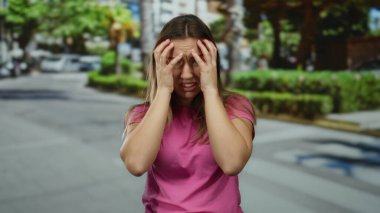 Sarı saçlı genç bir kadın güneşli bir şehir sokağında pembe bir gömlek giyerek strese giriyor ve hayal kırıklığı ve kafa karışıklığının çeşitli ifadelerini sergiliyor..