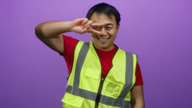 Güvenli bir yelek giyen genç adam canlı mor bir arka plana karşı neşeyle poz veriyor, pozitiflik ve ulaşılabilirlik taşıyor..