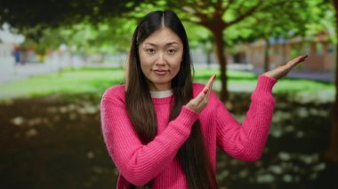 Pembe kazaklı kadın ağaçların altındaki parkta şaşkın şaşkın bakıyor güneş ışığı yaprakların arasından süzülüyor..