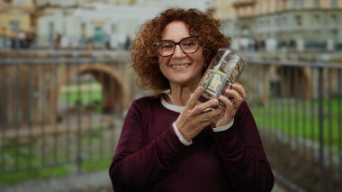 Roma harabelerinin önünde bir şişe dolarımızı tutarken gülümseyen bir kadın. Kültür, finans ve açık hava ortamında seyahat etmenin bir karışımını sergiliyor..
