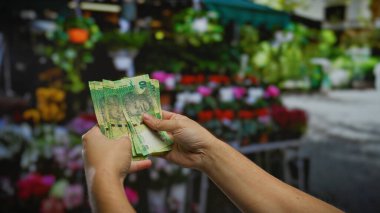 Güney Afrika Rand 'ini açık hava çiçekçisinde elinde tutan adam, harici bir ortamda para alım satımı ve para alışverişini vurguluyor..