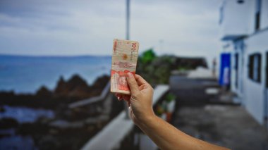 El ele tutuşarak Kolombiya pezosu sahil şeridinde, yerel para birimiyle tatil harcamalarını ve manzaralı bir plaj arkaplanını vurguluyor..