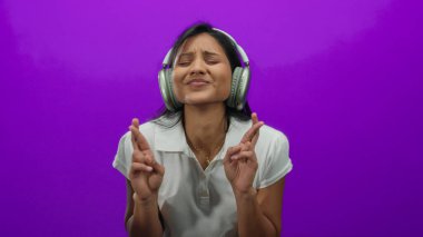 Kulaklık takan, parmakları parlak mor bir arkaplan üzerinde umut ve pozitifliği ifade eden neşeli tavırlı, sıradan beyaz bir gömlek giyen bir kadın..