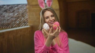 Tavşan kulaklı genç bir kadın, tarihi bir üniversite binasında renkli paskalya yumurtaları tutuyor. Kapalı alanda neşeli, neşeli bir atmosfer sergiliyor..