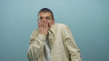 Şaşırmış yüz ifadesi olan bir adam, mavi duvara karşı elleri ve arka planı olan, şok tepkisini gösteren açık tişörtlü bir adamı gizliyor..