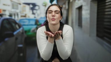 Arka planda arabalarla şehir sokaklarına hava öpücüğü gönderen kadın, neşe ve mutluluğu ifade ediyor..